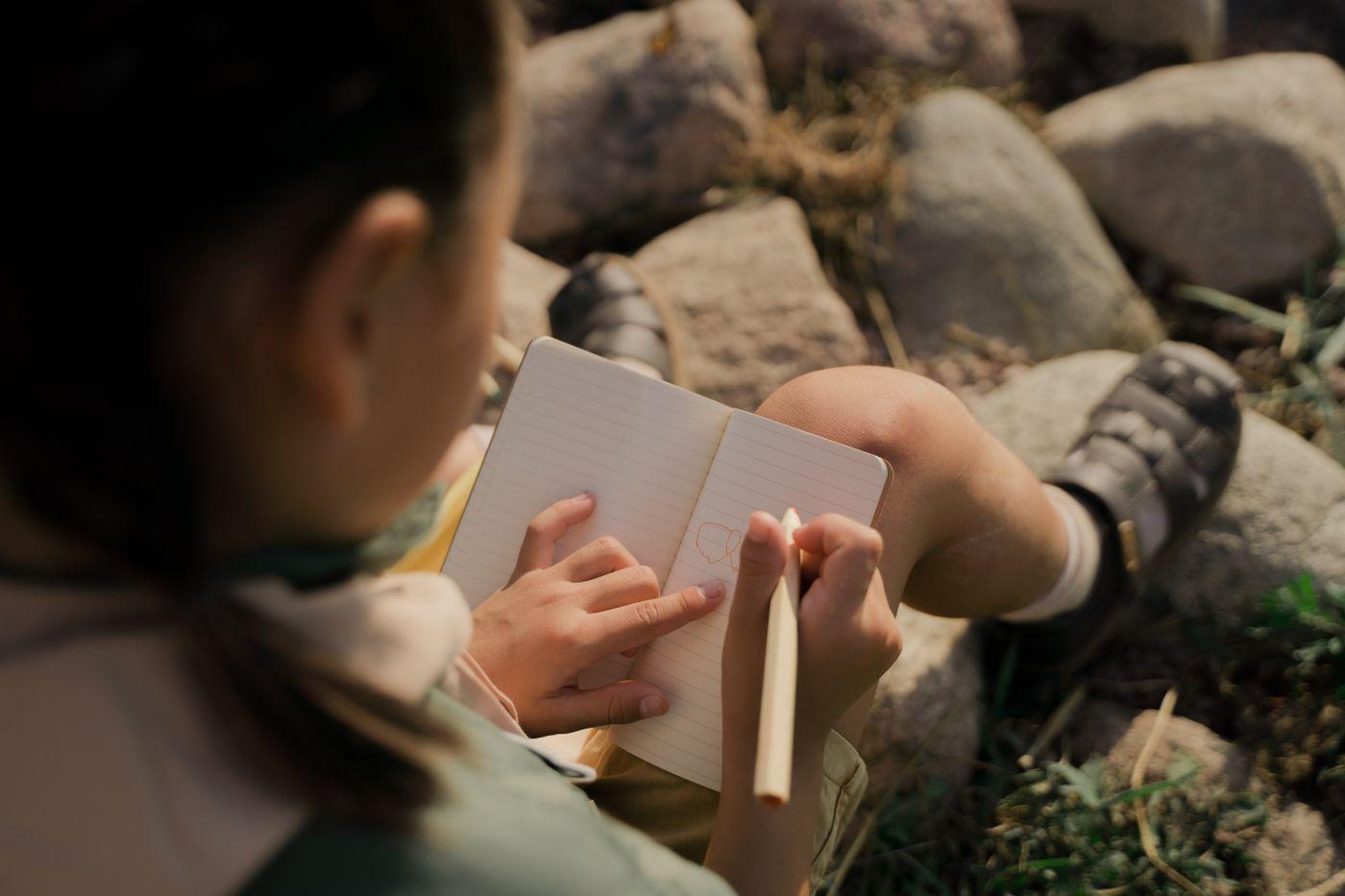 A young learner writing quietly outdoors in nature